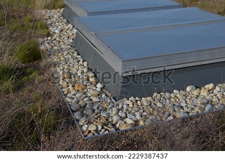 metal grates and a hatch on the roof garden. sheet metal and metal covering the entrances to the back of the cooling units. the area around the door is mulched with pebbles. against fire edge