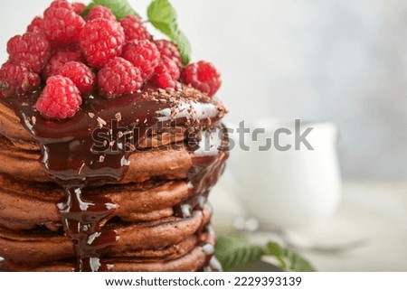 Chocolate Pancakes. Pancakes with fresh raspberry with chocolate glaze or toppings in gray bowl on light gray table background. Homemade classic american pancakes. Page for magazine concept.