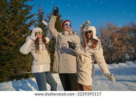 Outdoor winter activities. Happy friends a guy and girls have an active rest and rejoice in a winter park on a sunny day. Winter fashion. Good mood, emotions. 