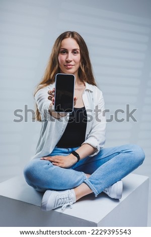 Young woman with long brunette hair, wearing a white shirt and jeans, having a video call conversation on the phone. A woman in jeans and a plain white shirt with a mobile phone. White background