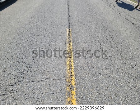 A faded yellow line in the center of a cracked concrete road.