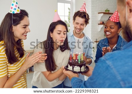 Happy birthday, girl. Quick, make a wish. Group of happy diverse mixed race friends enjoying a birthday party. Young woman who is in her 20s is blowing the candles on her birthday cake
