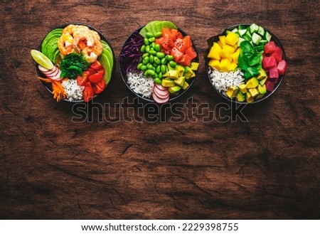 Hawaiian poke bowl set: tuna, salmon, shrimp with avocado, mango, radish, rice and other ingredients. Soy sauce and sesame dressing. Wooden table background, copy space, top view