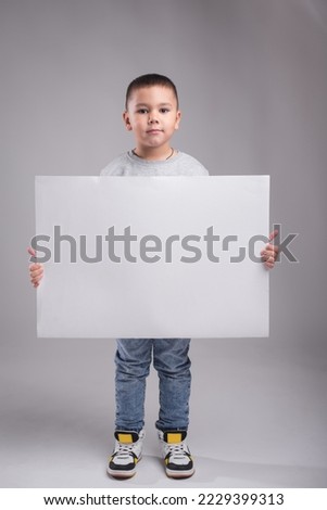 The boy is holding a large white sheet of paper. Child on a white background with a board for an inscription. Place for text on the background of the child.