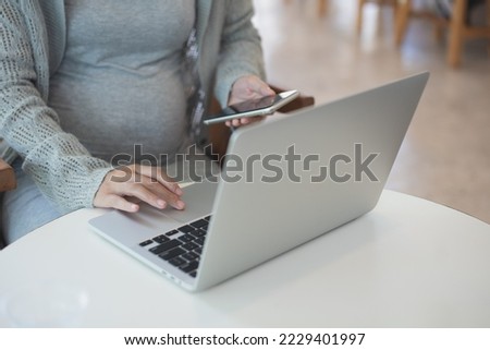 Pregnant business woman sitting at table using mobile phone and working on laptop computer at cafe. pregnant woman online shopping via mobile app, close up