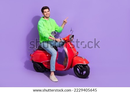 Full length photo of satisfied cool guy with brunet hairdo dressed green hoodie directing empty space isolated on purple color background