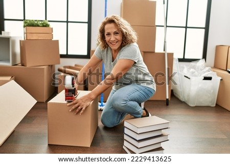 Middle age caucasian woman smiling happy packing carboard box at new home. Royalty-Free Stock Photo #2229413625