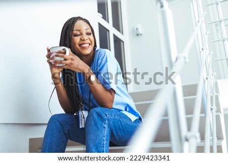 Female doctor sitting with mobile phone and drinking coffee.  Pretty female nurse drinking coffee and rest after hard work. People, profession and healthcare concept. 