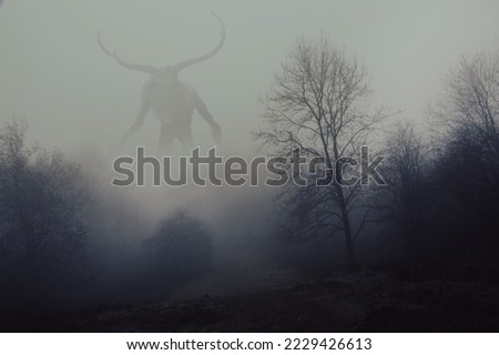 A fantasy concept of a horned god like monster. Looking across a forest on a spooky foggy, winters day.  Royalty-Free Stock Photo #2229426613