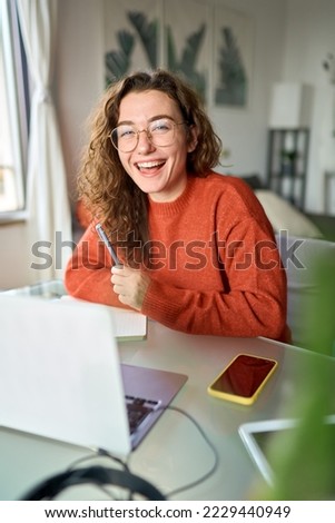 Happy young woman student laughing using laptop sitting at desk studying online, looking at camera. Elearning concept. Virtual education classes, remote work and business webinars. Vertical portrait.