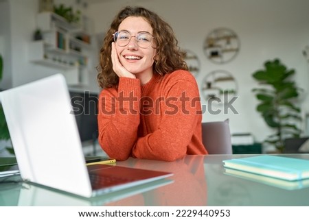 Young happy pretty business woman student sitting at desk at home office with laptop computer looking at camera advertising online learning, remote work, business webinars. Portrait.