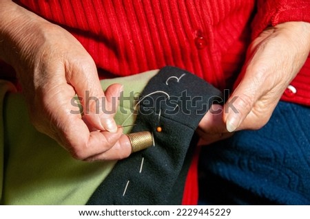 Close up mature woman hands sewing with needle and thread. Royalty-Free Stock Photo #2229445229