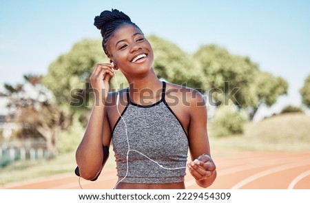 Earphones, fitness and black woman running on a track for marathon, race or competition training. Sports, workout and athlete runner listening to music, radio or podcast while doing cardio exercise. Royalty-Free Stock Photo #2229454309