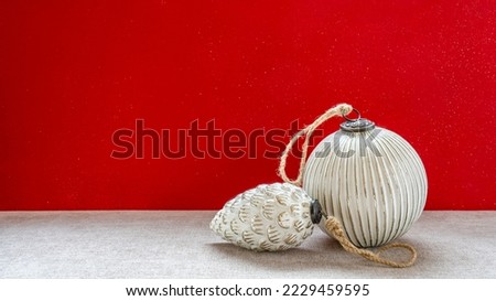 Two vintage Christmas baubles with string against a red background
