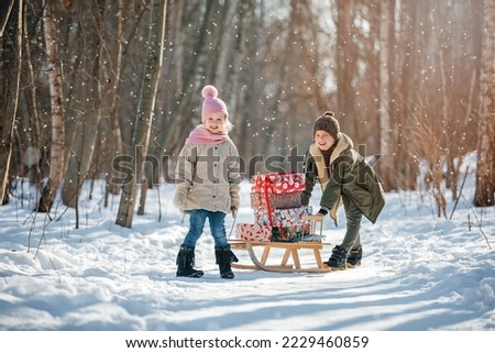 A little girl and boy carry the sledge with Christmas presents, on winter background