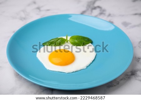 Tasty fried egg with basil in plate on white marble table, closeup