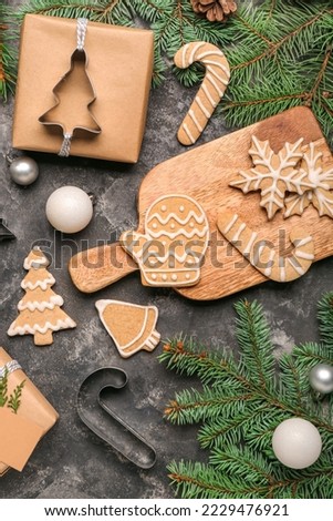 Wooden board with tasty Christmas cookies, gift and fir branches on dark background Royalty-Free Stock Photo #2229476921