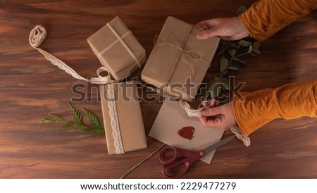 Two hands with orange long sleeve shirt picking a kraft box surrounded by more boxes