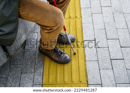 Close-up of a blind man with a cane sits on a bench in the city near the tactile tiles