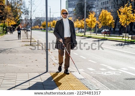 Blind man with a walking stick. Walks on tactile tiles for self-orientation while moving through the streets of the city Royalty-Free Stock Photo #2229481317