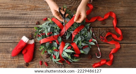 Hands of woman making Christmas wreath on wooden background, top view