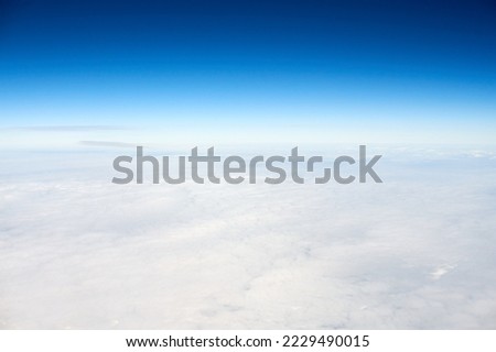 Over clouds aerial top view from aircraft window, thick white blue clouds looks like soft foam, overcast with fresh frosty air. Beautiful cloudy sky view to troposphere, heavy cloudiness Royalty-Free Stock Photo #2229490015