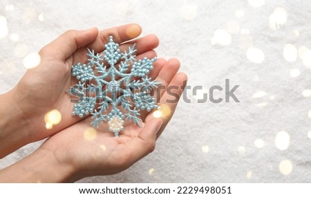 Female hands holding snowflake on light background, closeup