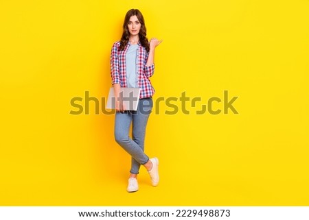 Full length photo of attractive young business lady hold netbook finger point new it company advert empty space isolated on yellow color background
