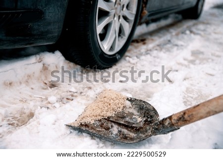 Shovel with salt on snowy driveway to protect from slippery. Winter snow cleaning the road outside. Applying Rock Salt ( Gritting ) to an Icy road for safe car traffic. De icing Copy space Royalty-Free Stock Photo #2229500529