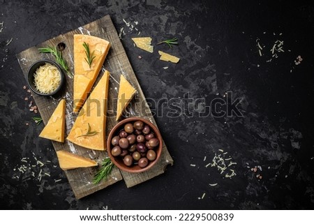 Parmesan cheese on a wooden board, Hard cheese, olives, rosemary on a dark background. place for text, top view, Royalty-Free Stock Photo #2229500839