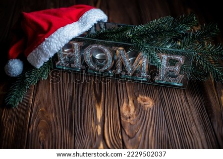 Christmas card. Word House is made of shiny glass letters on a wooden background decorated with spruce branches. Santa Claus' Red Hat. New Year's vintage background.