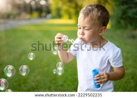 cute blonde baby inflates soap bubbles in summer on a green lawn, having fun, outdoor recreation