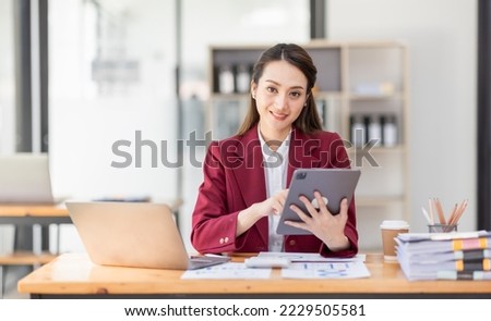 Asian woman working laptop in workplace, Business woman wearing red jacket suit busy working on laptop computer checking finances, investment, economy, saving money or insurance concept Royalty-Free Stock Photo #2229505581