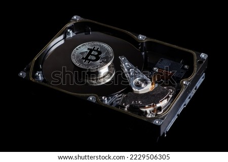 Silver Bitcoin coin on the opened HDD disk on black background. Electronic money, cryptocurrency.