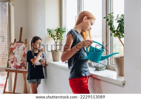 Diligent and beautiful teenagers clean houses, wash windows and dust. Lovely girls love to take care of plants and water them on a spacious light windowsill. A teenager sprays flowers at home.
