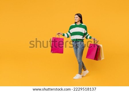Full body young latin womanwear casual cozy green knitted sweater hold in hand paper package bags after shopping walk go isolated on plain yellow background studio. Black Friday sale buy day concept