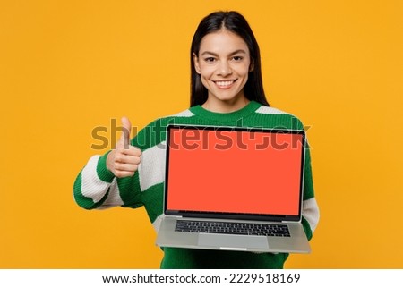 Smiling young latin IT woman wear casual green knitted sweater hold use work on laptop pc computer with blank screen workspace area show thumb up isolated on plain yellow background studio portrait