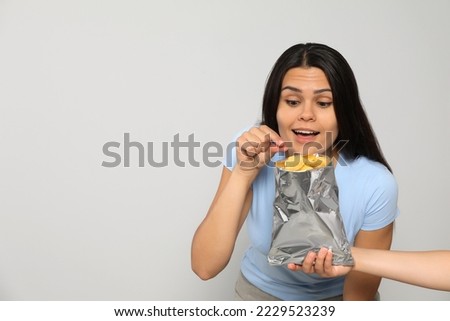 Beautiful young woman eating tasty potato chips on grey background, space for text