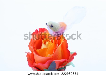 A fake bird and orange textile rose flower