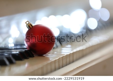 Beautiful red bauble and fairy lights on piano keys, space for text. Christmas music