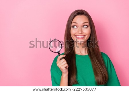 Photo of gorgeous adorable pretty girl dressed green t-shirt look empty space hold magnifying glass isolated on pink color background