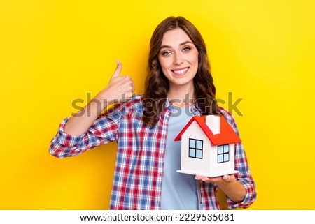 Photo of pretty cute lady wear plaid shirt open thumb up holding arms little red roof house isolated yellow color background