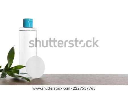 Micellar water in bottle and cotton pads on wooden table against white background. Space for text