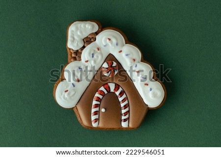 Christmas gingerbread house shaped cookie with white snow icing on a green background. Homemade festive traditional cookies. Merry Christmas greeting