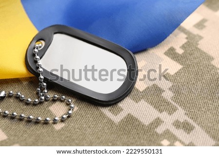 Military ID tag and Ukrainian flag on pixel camouflage, closeup
