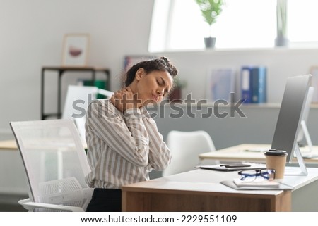 Neck pain. Exhausted young female entrepreneur massaging aching neck, suffering from ache, sitting at workplace in office. Osteoarthritis, health problem, sedentary lifestyle concept Royalty-Free Stock Photo #2229551109