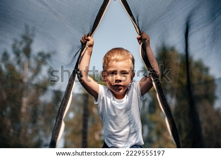 A cute little boy jumps on a new trampoline in the summer in the village and laughs. A happy child enjoys a new trampoline