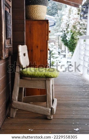 Terrace of a wooden house overlooking the winter forest. On the terrace there is a wooden chair with a green cushion. Vertical photo