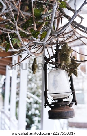 On the terrace of a wooden house hangs an old lantern lantern with a decor of dry branches. Vertical photo