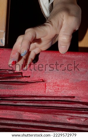 Hand of a painter stained with paint touching a red drawing in a canvas